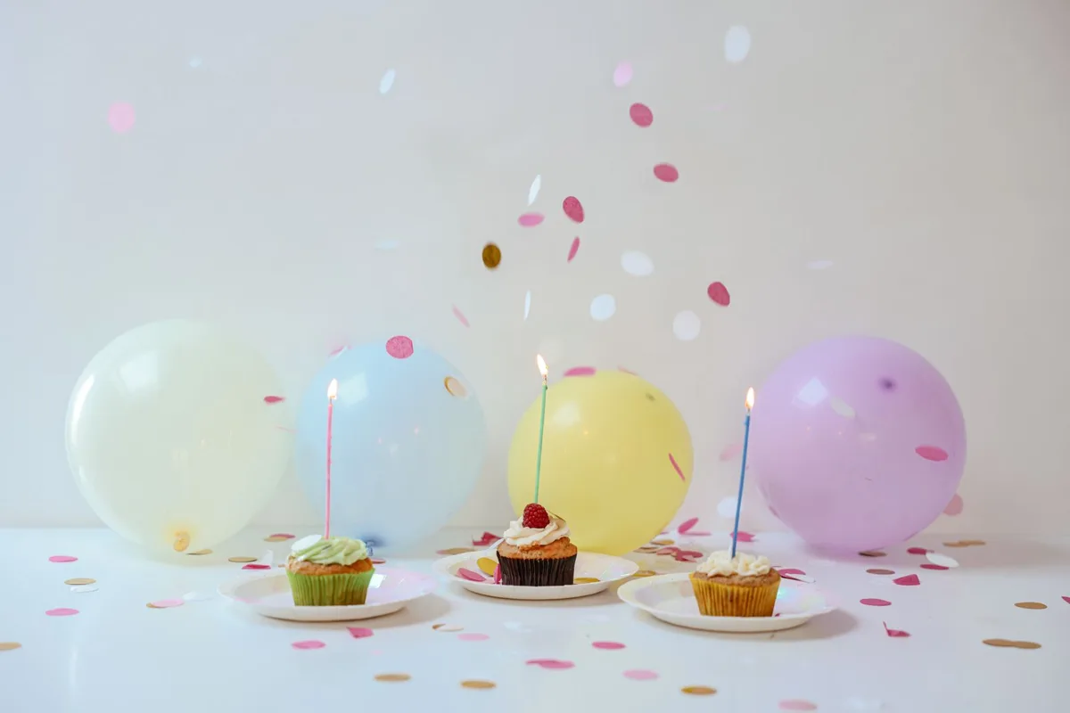 Cupcakes with lit birthday candles on a celebration table with balloons